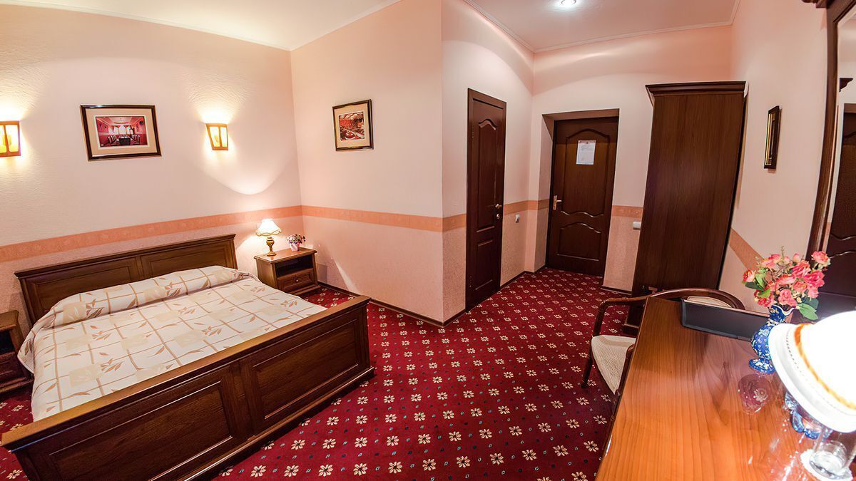 Una habitación de hotel con una cama de madera, una mesita de noche con una lámpara, un escritorio con un florero y un espejo.