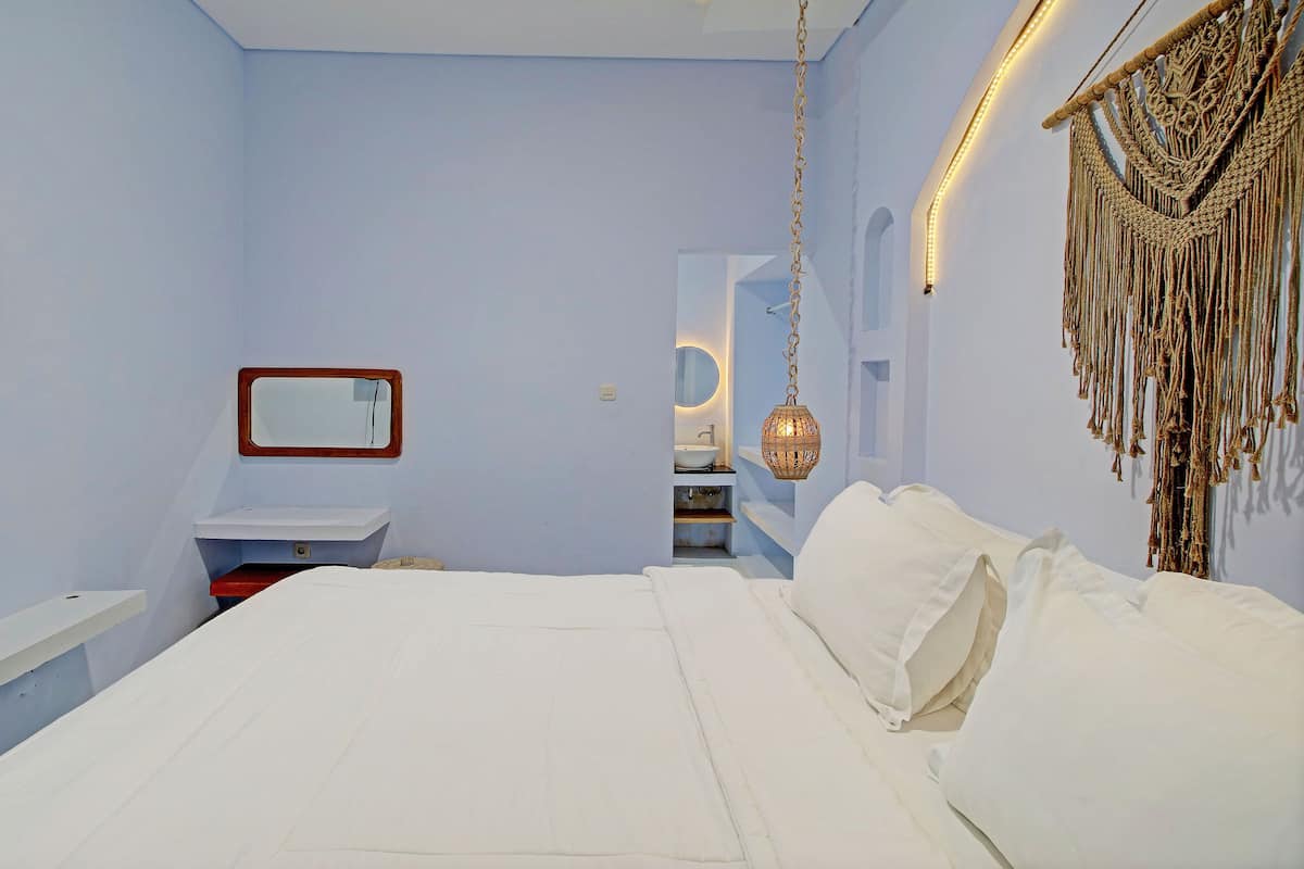 A bedroom with a bed, a bedside table, a mirror, and a wall-mounted macrame piece.