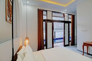 A modern hotel room with a large bed, a wooden nightstand, a hanging lamp, and a view of the outside balcony. - Collection O 93004 Double D Guest House (Perean Tengah)