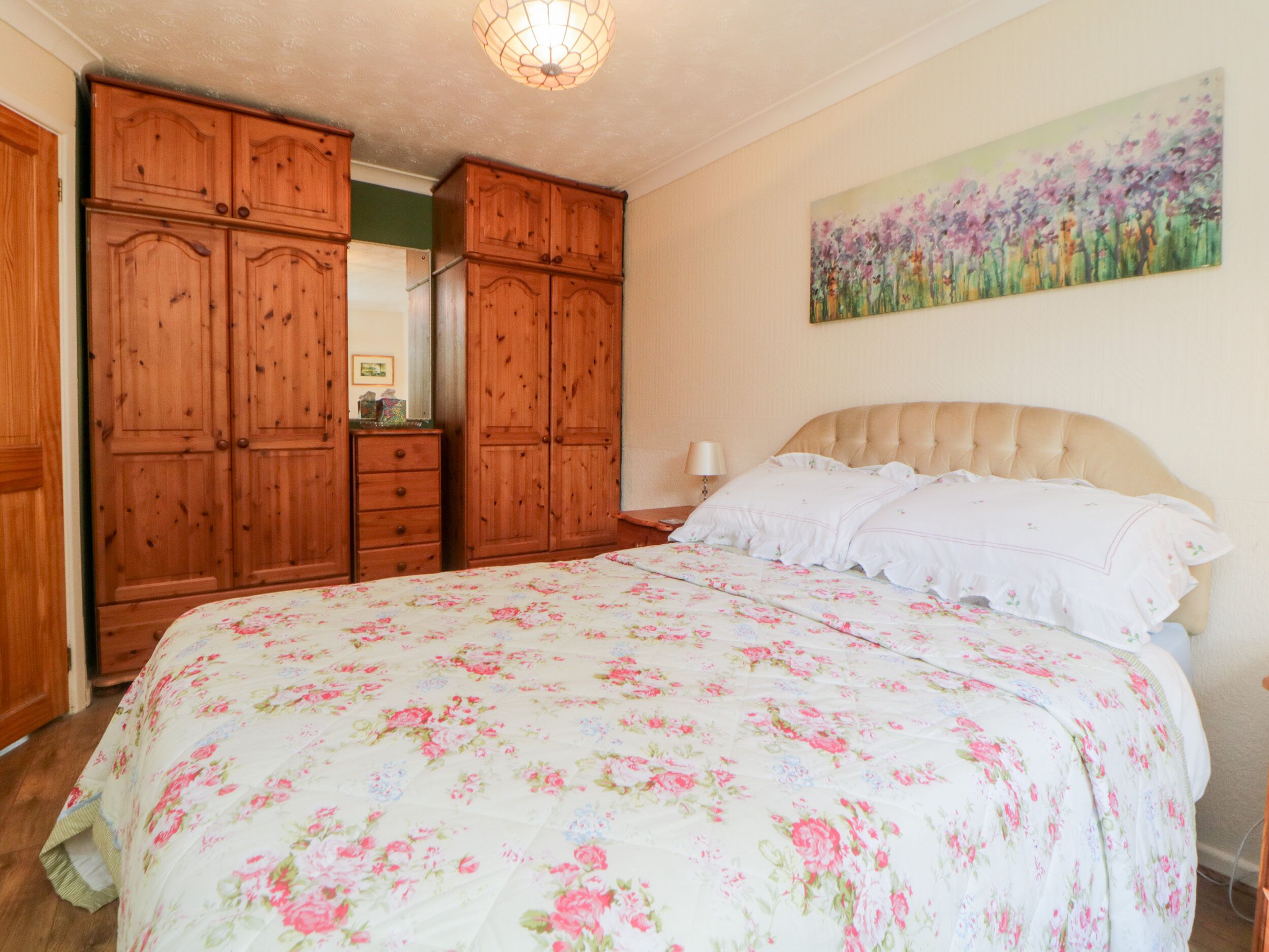 A bedroom with a large bed, wooden wardrobe, and a painting on the wall.