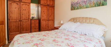 A bedroom with a large bed, wooden wardrobe, and a painting on the wall.