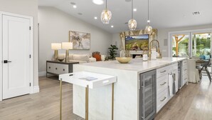 A modern kitchen with a marble island, pendant lighting, and a view of the outdoors. - Elegant Renovated Home W/ Backyard Misters & Pool (Phoenix)