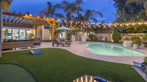 A backyard with a swimming pool, artificial grass, outdoor furniture, and string lights. - Elegant Renovated Home W/ Backyard Misters & Pool (Phoenix)