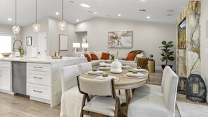 A modern kitchen with white cabinetry, a dining area with a round table, and a living room with a sofa and coffee table. - Elegant Renovated Home W/ Backyard Misters & Pool (Phoenix)