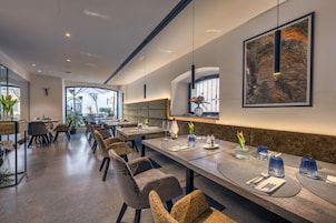 A modern dining area with long tables, comfortable chairs, and pendant lighting.