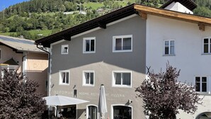 A building with multiple windows, outdoor seating, and a sign indicating rooms, restaurant, and pizzeria. - Nepomuk (Vipiteno)