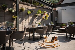 An outdoor dining area with multiple tables and chairs, potted plants on a wall, and a rocking horse.