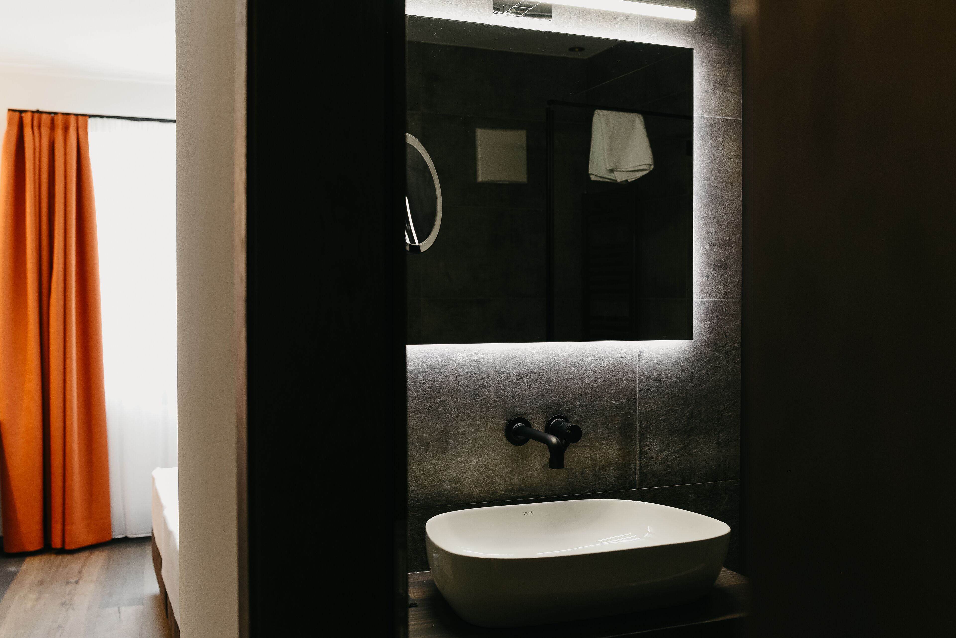 Une salle de bain moderne avec un grand miroir, un lavabo blanc et une serviette accrochée au mur.