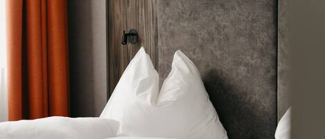 Una cama bien hecha con ropa blanca y almohadas, cabecera de madera y cortinas anaranjadas.
