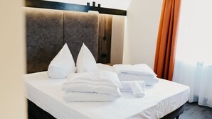 A neatly made bed with white linens and pillows, a wooden headboard, and a window with orange curtains. - Nepomuk (Vipiteno)