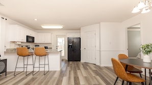 A modern kitchen with white cabinets, a black refrigerator, and wooden flooring. - Comfortable 3BR | Screened Patio + Grill | WR (Warner Robins)