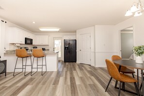 A modern kitchen with white cabinets, a black refrigerator, and wooden flooring.
