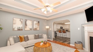 A living room with a sofa, a round coffee table, a fireplace, and a kitchen visible through an archway. - Comfortable 3BR | Screened Patio + Grill | WR (Warner Robins)