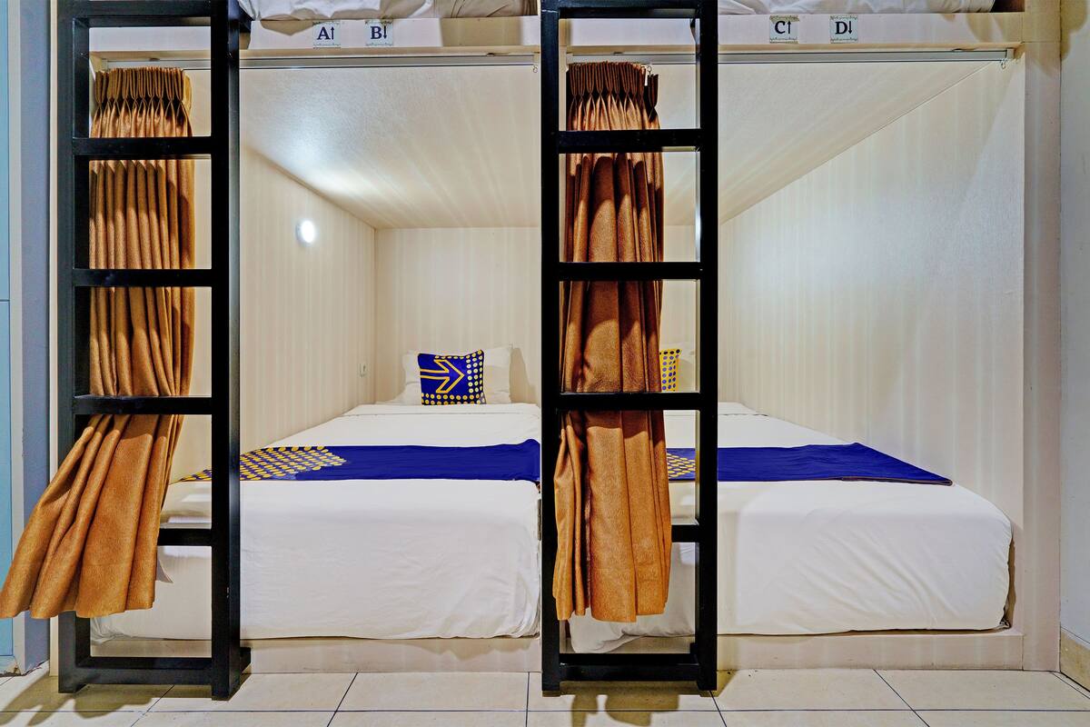 A room with two beds, each with a blue and yellow checkered pillow, and a brown curtain on a black frame.