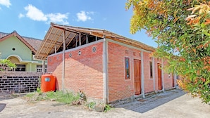 Un bâtiment en briques avec un toit en construction partielle, une porte rouge et une petite fenêtre.