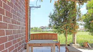 Un banc et une table en bois sont placés contre un mur de briques, et offrent une vue sur un champ verdoyant et des arbres en arrière-plan.