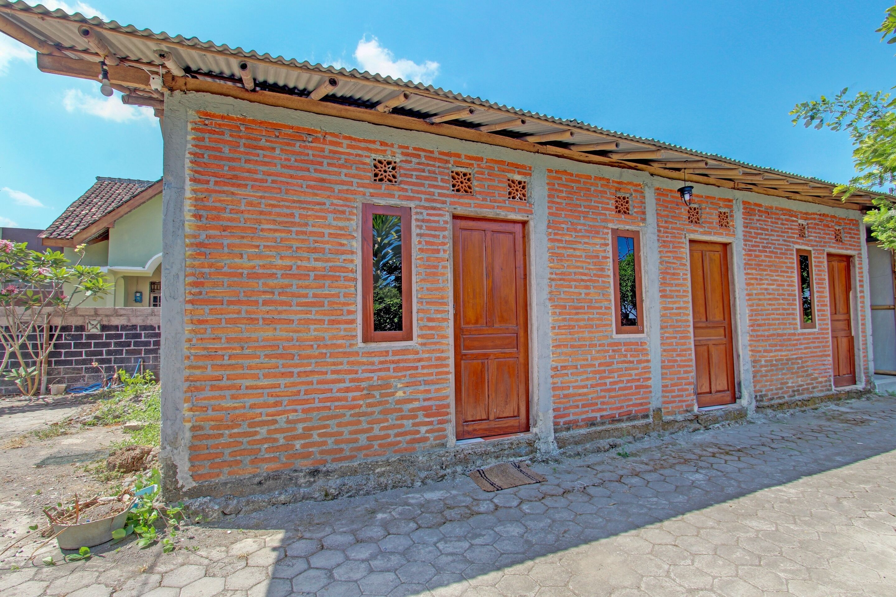A brick building with wooden doors and windows, a tiled roof, and a paved walkway.