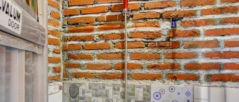 A bathroom with a brick wall, a shower with a red handle, and a tiled floor.