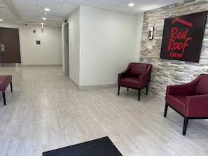 A hotel lobby with a reception desk, two red armchairs, a black rug, and a wall sign for Red Roof Inn.