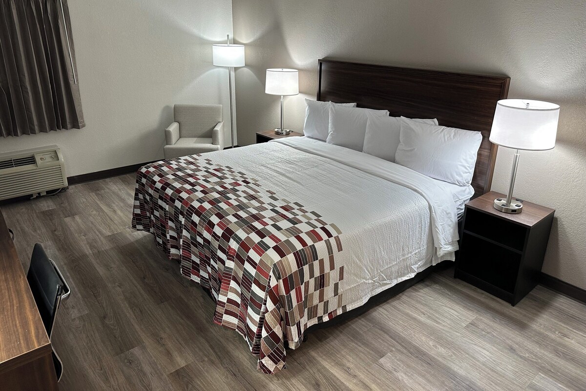 A hotel room with a large bed, two bedside lamps, a chair, a desk, and a heater.