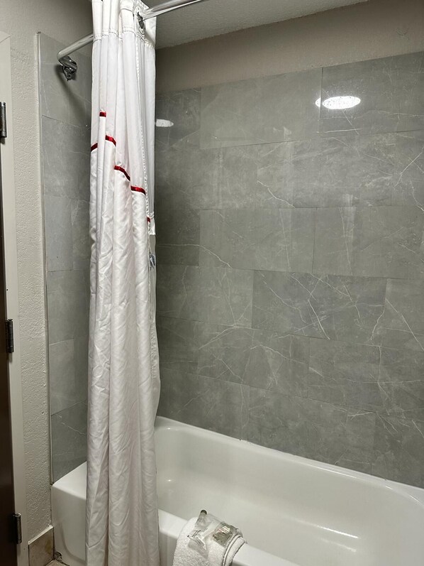 A bathroom with a bathtub, a shower curtain, and grey marble tiles. - Red Roof Inn Charleston - Dunbar (Dunbar)
