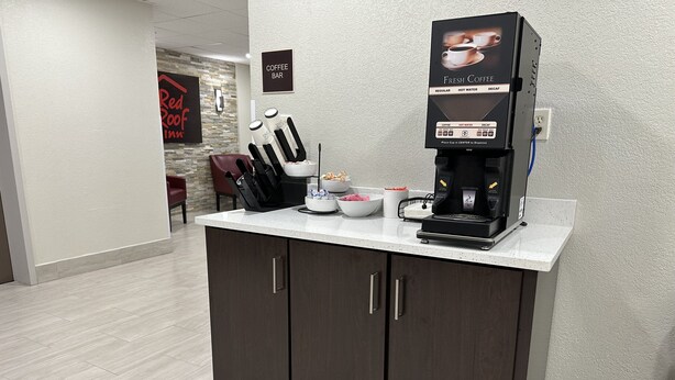 A coffee bar with a coffee machine, cups, and a sign indicating it is a coffee bar. - Red Roof Inn Charleston - Dunbar (Dunbar)