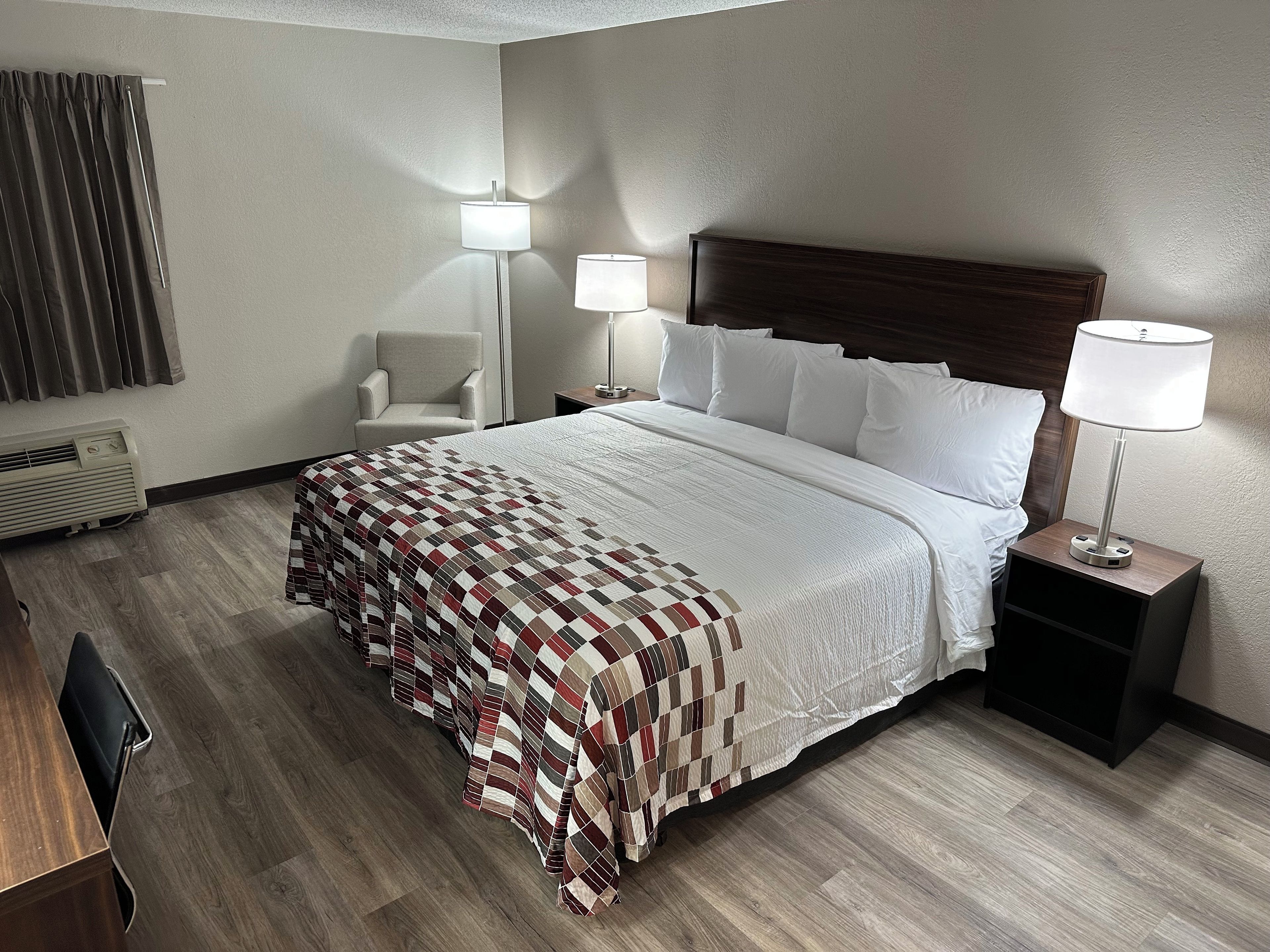 Una habitación de hotel con una cama grande, dos lámparas de noche, una silla y un escritorio.