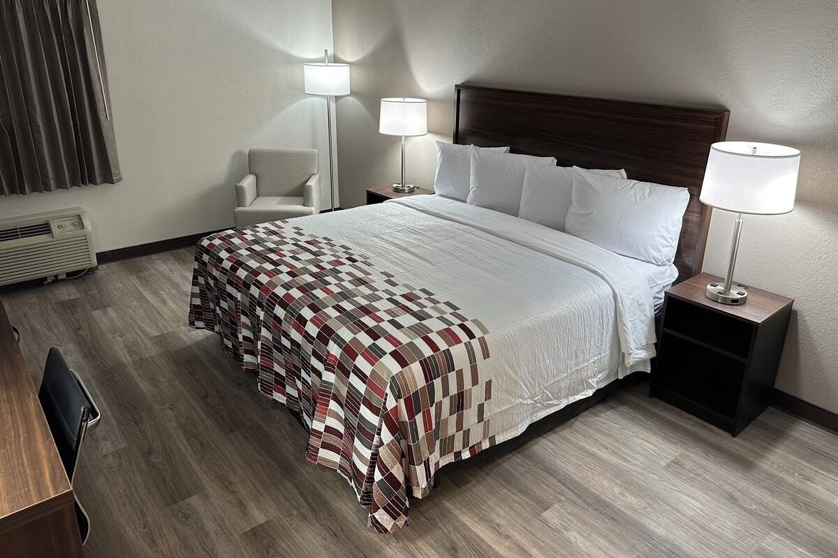 A hotel room with a large bed, two bedside lamps, a chair, a desk, and a heater.