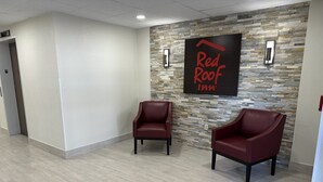 A hotel lobby with a stone wall, two red leather chairs, and a 'Red Roof Inn' sign. - Red Roof Inn Charleston - Dunbar (Dunbar)