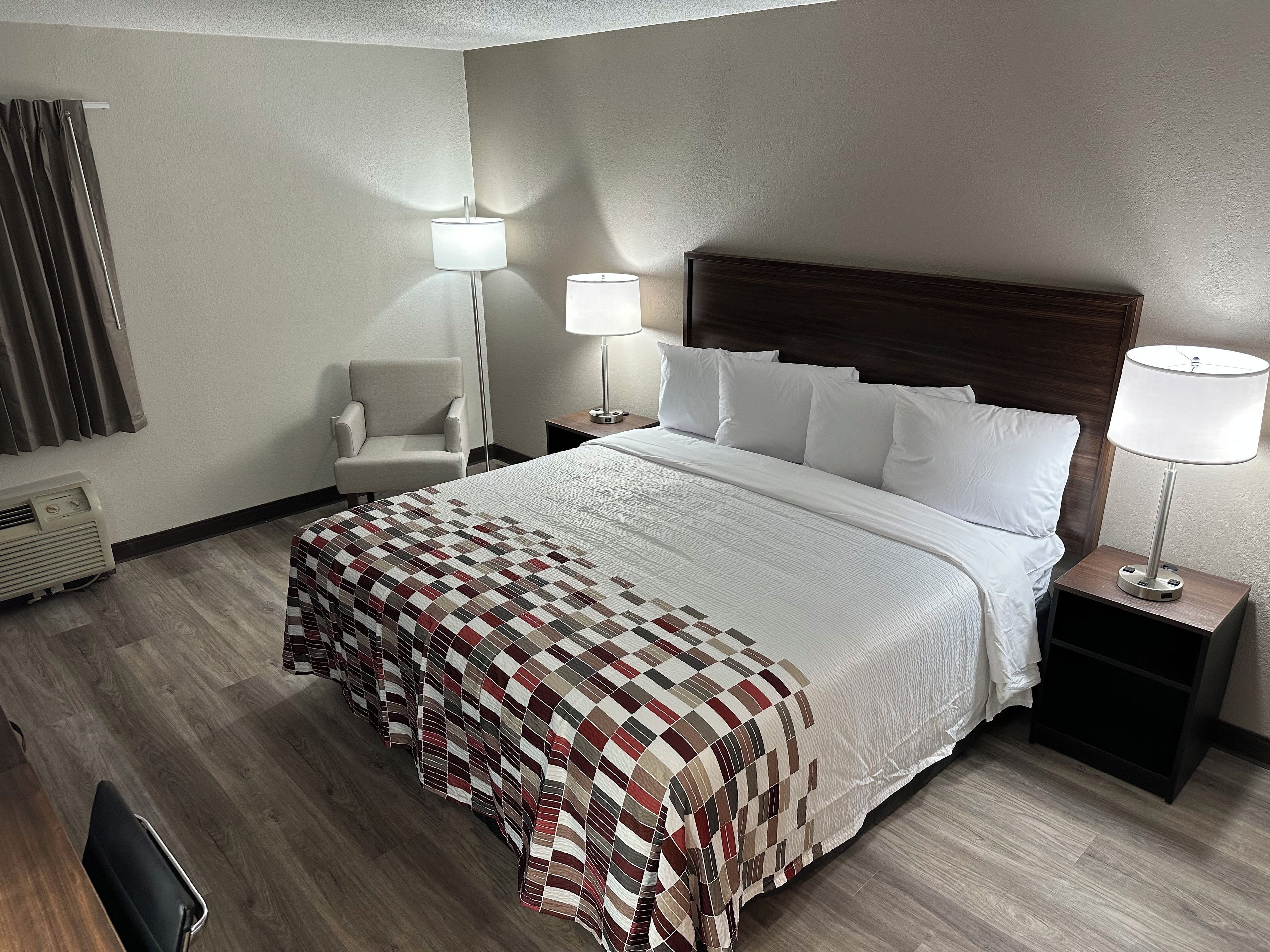 A hotel room with a large bed, two bedside tables with lamps, a chair, and a heater.