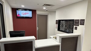 A reception area with a TV displaying a welcome message, a check-in/out time sign, and a notice about room items. - Red Roof Inn Charleston - Dunbar (Dunbar)