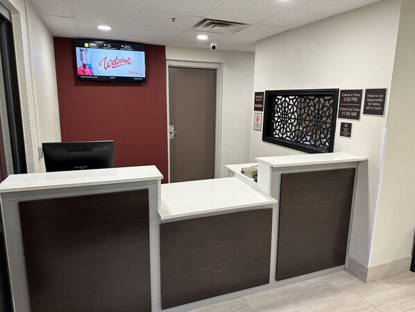 A reception area with a TV displaying a welcome message, a check-in/out time sign, and a notice about room items. - Red Roof Inn Charleston - Dunbar (Dunbar)