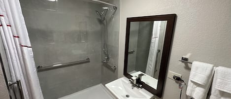 A bathroom with a glass-enclosed shower, a white sink, and a mirror with a wooden frame.