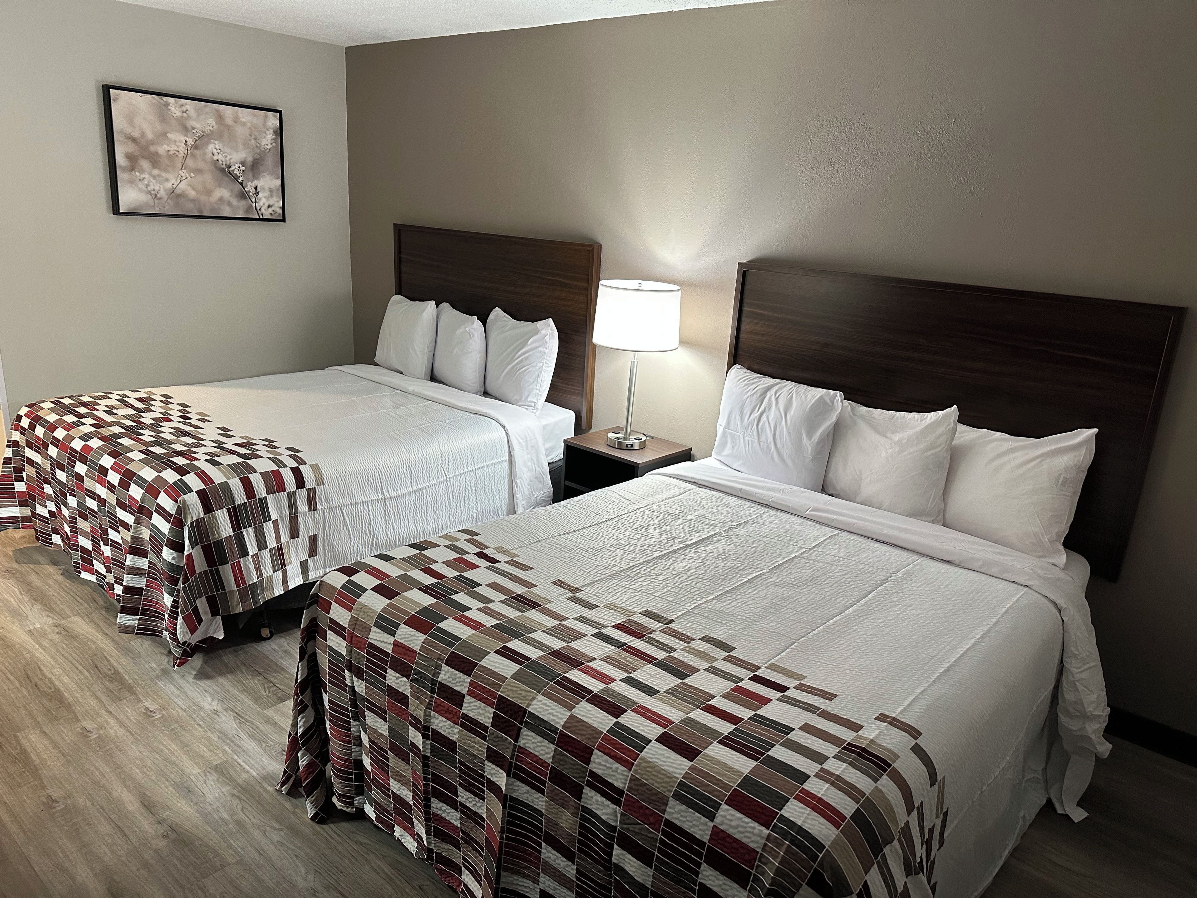 A hotel room with two beds, a nightstand with a lamp, and a framed picture on the wall.