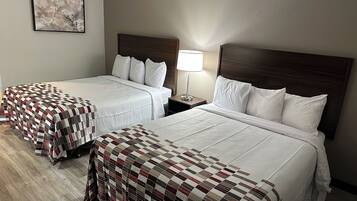 A hotel room with two beds, a nightstand with a lamp, and a framed picture on the wall.