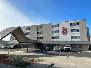 A Red Roof Inn with a modern architectural design, featuring a parking lot with several cars and a covered walkway.