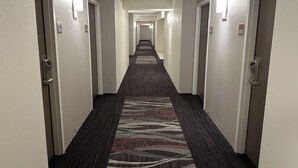 A hotel hallway with carpeted floors, doors on both sides, and wall-mounted light fixtures. - Red Roof Inn Charleston - Dunbar (Dunbar)