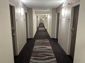 Pasillo de hotel con pisos alfombrados, puertas a ambos lados e iluminación empotrada en las paredes.