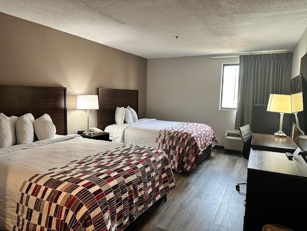 Habitación de hotel con dos camas, un escritorio y una ventana con cortinas.