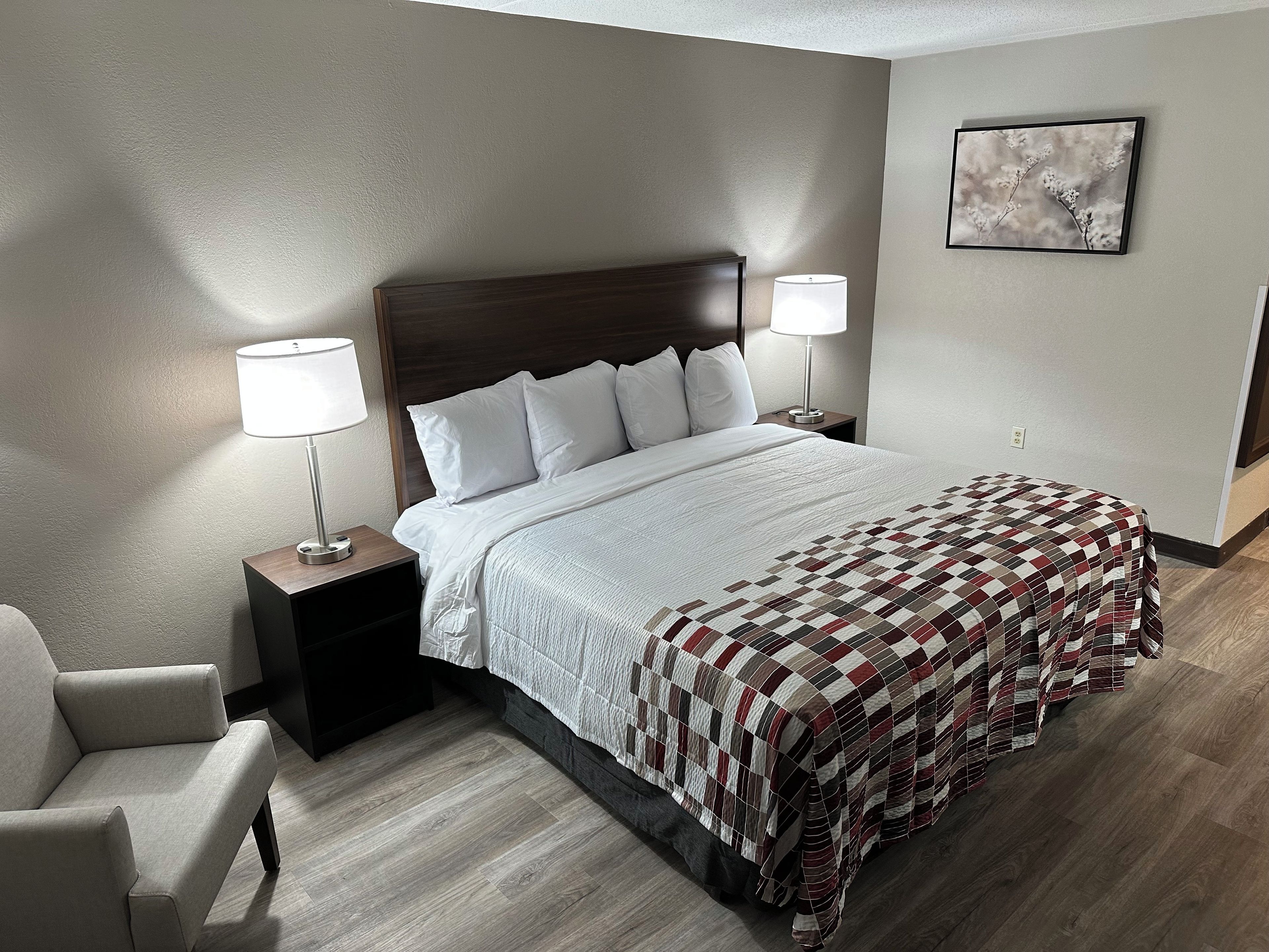 A hotel room with a large bed, two bedside tables with lamps, a chair, and a wall-mounted picture.