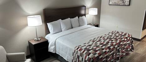 A hotel room with a large bed, two bedside tables with lamps, a chair, and a wall-mounted picture.