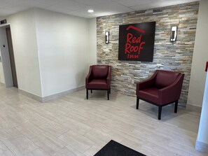 Un hall d’entrée de Red Roof Inn avec un mur en pierre, deux fauteuils en cuir et un tapis noir.