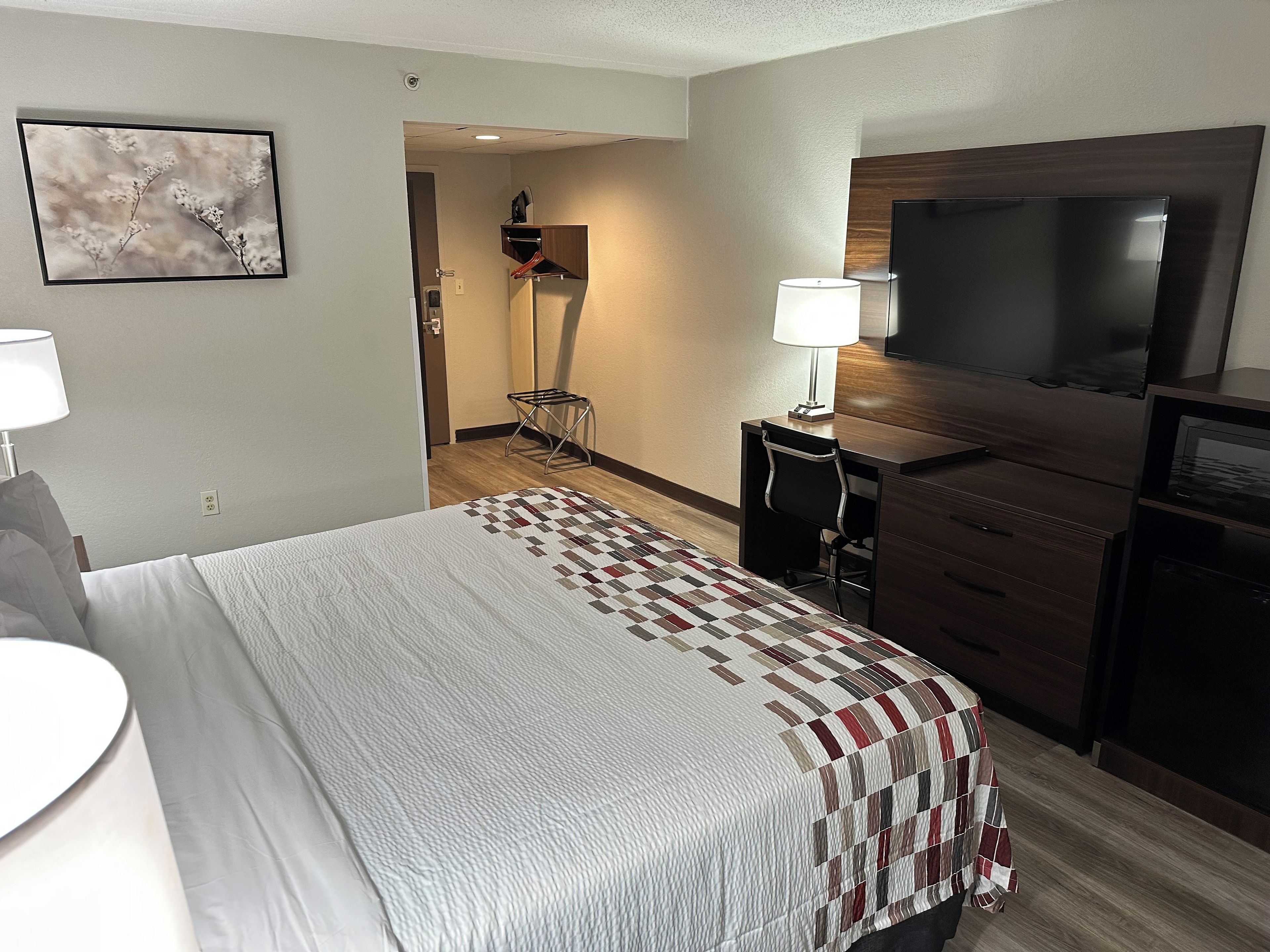 Una habitación de hotel con cama, escritorio, silla, televisor y lámpara.