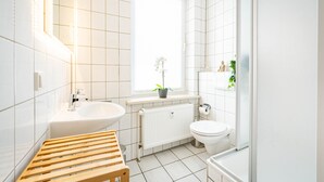 A modern bathroom with a wooden bench, a sink, a toilet, and a window with a plant.