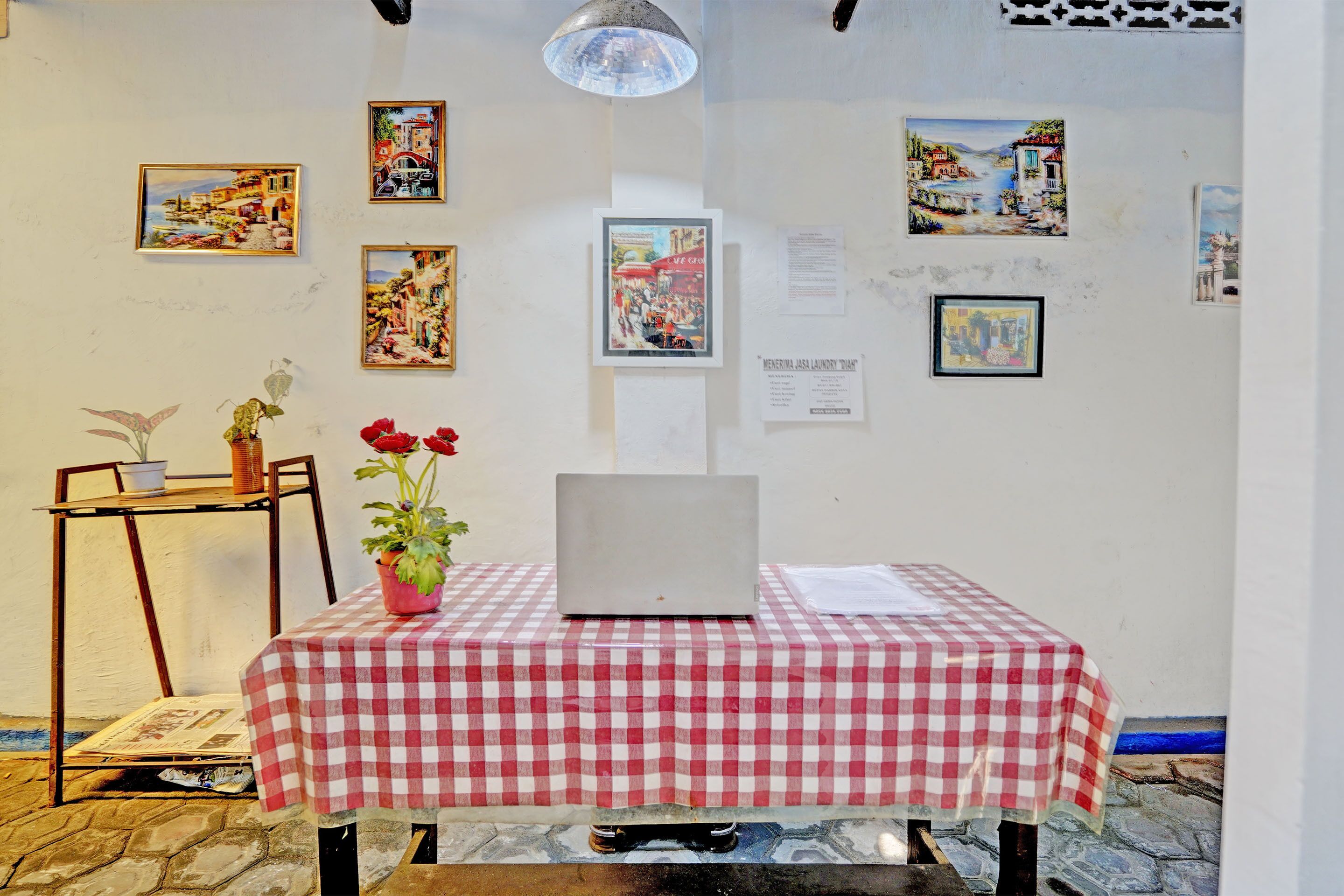 A room with a checkered tablecloth, a laptop, and various framed artworks on the walls.