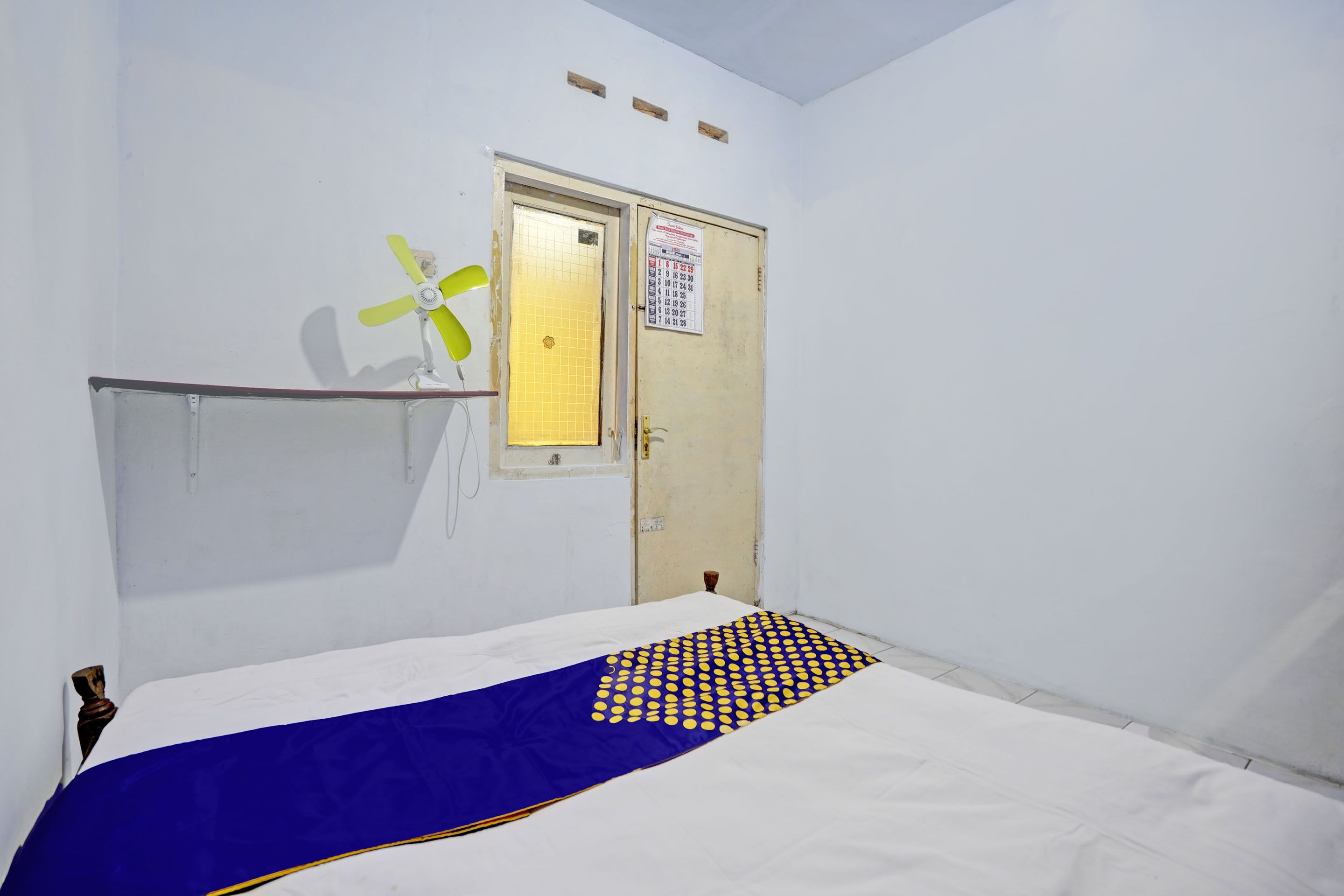 A room with a bed, a door with a calendar, and a ceiling fan.