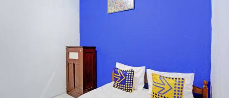 A bedroom with a blue wall, a wooden wardrobe, and two beds with patterned pillows.