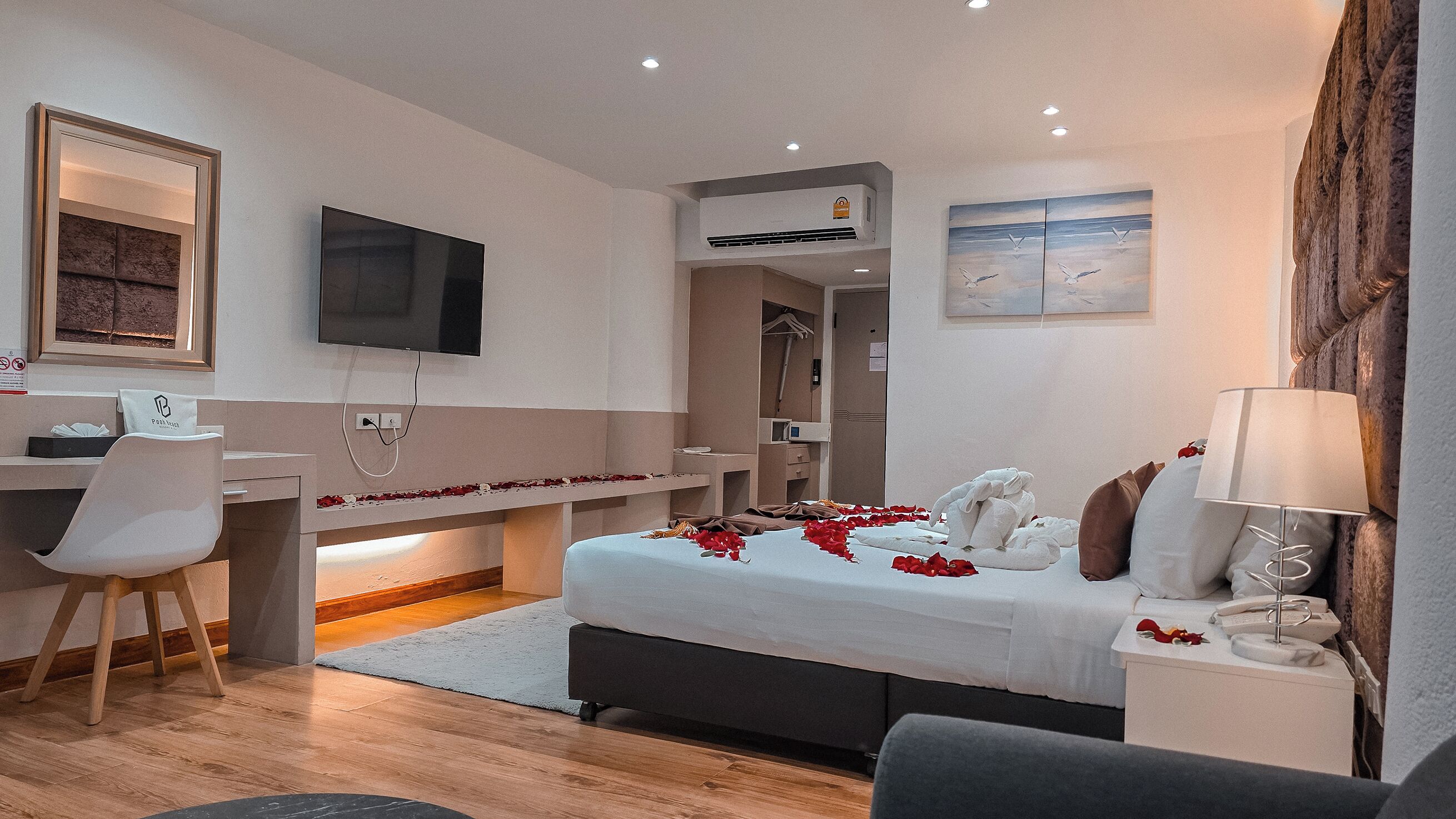A hotel room with a bed, bedside table, lamp, TV, desk, chair, and a mirror.