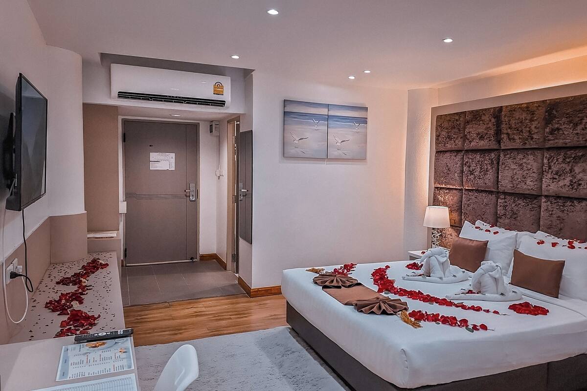 A hotel room with a bed, bedside table, lamp, and a television on the wall.
