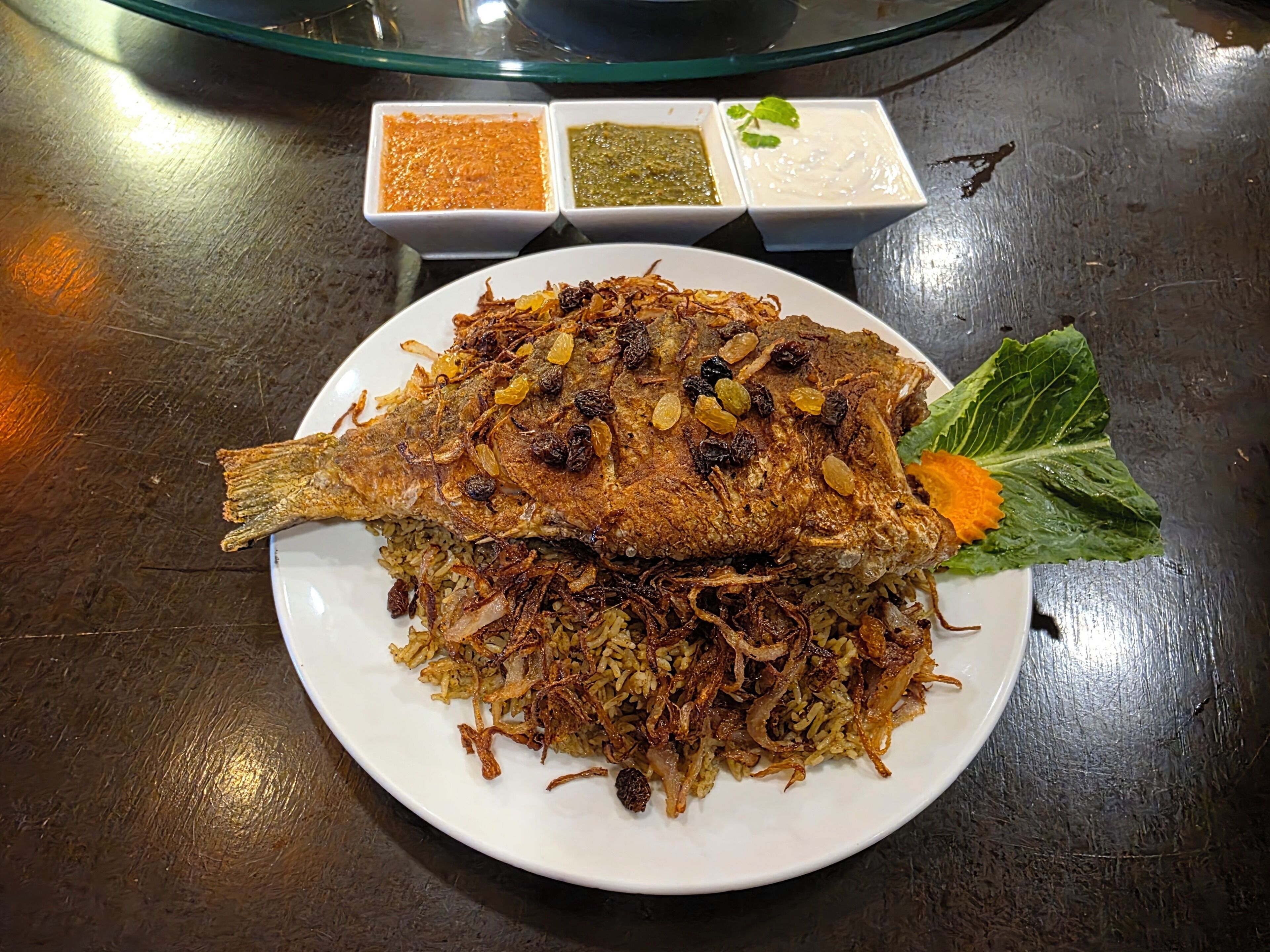 Une assiette de poisson frit, servie avec du riz et des oignons frits, accompagnée de trois petits ramequins de sauces.
